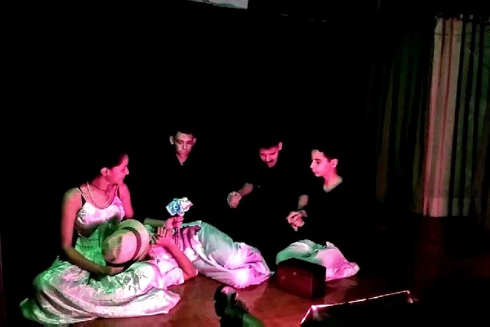 Grupo de intérpretes participa en una escena teatral colectiva bajo iluminación escénica.